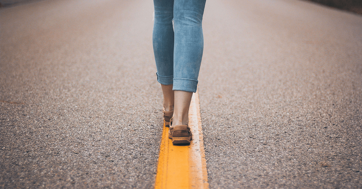 Woman walking on a line in the middle of the road; image representing risk appetite