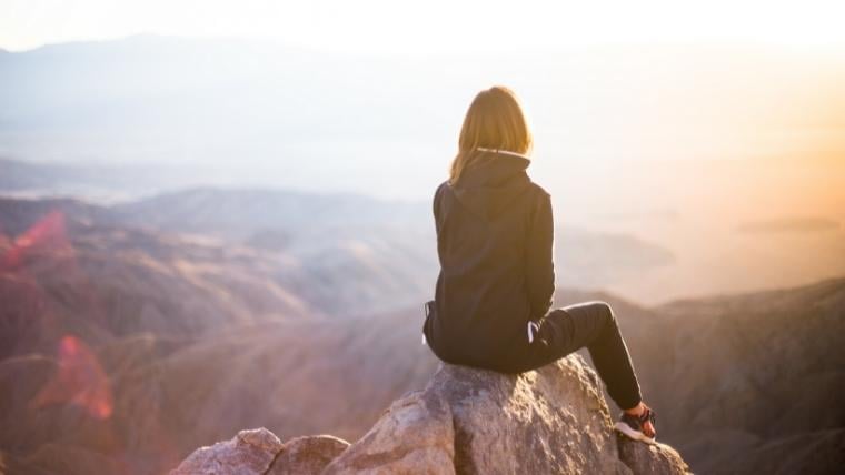 Opportunity risk management blog - woman sitting on a mountaintop rock looking down at valley